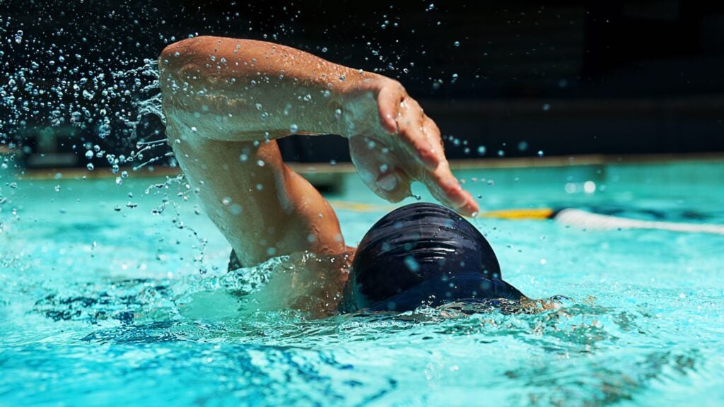 Pool, water splash and athlete swimming in sport for competition, race or training in cardio. Fitness, workout and person exercise for health, wellness or practice stroke or performance in the Epic pool.